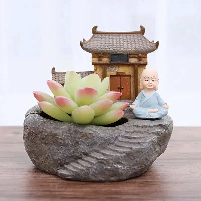 a small buddha statue sitting on top of a rock next to a succulent