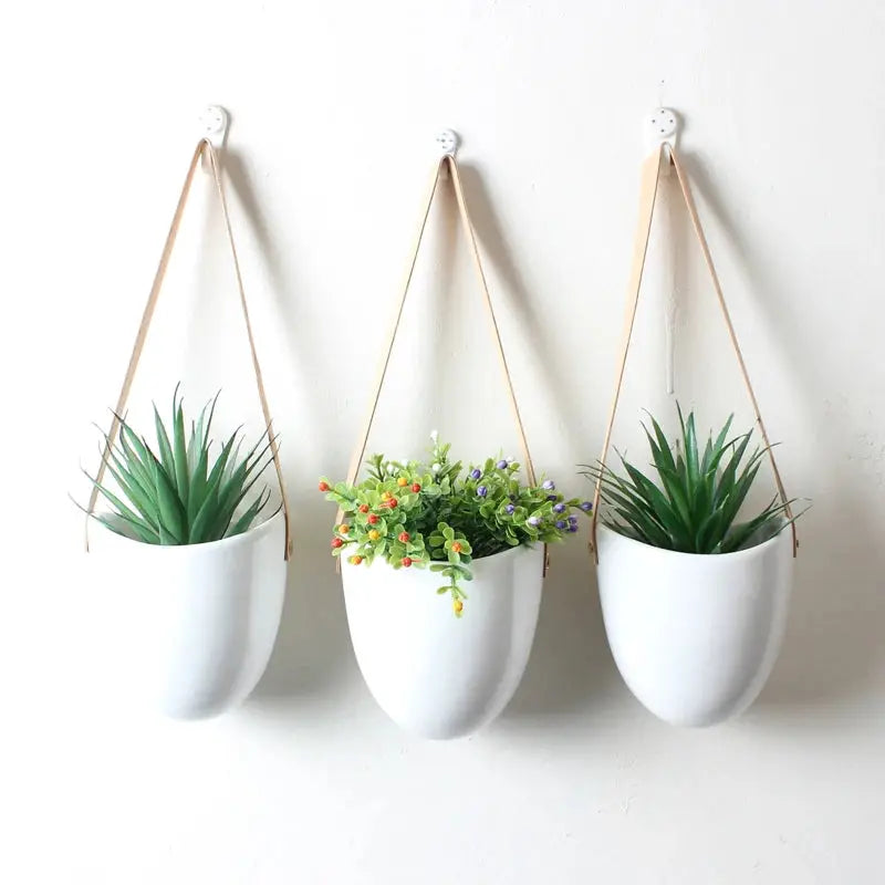 three white hanging planters with plants in them