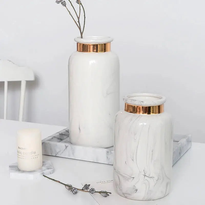 two white vases sitting on top of a table next to a candle