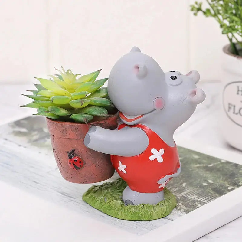 a small statue of a hippo holding a potted plant