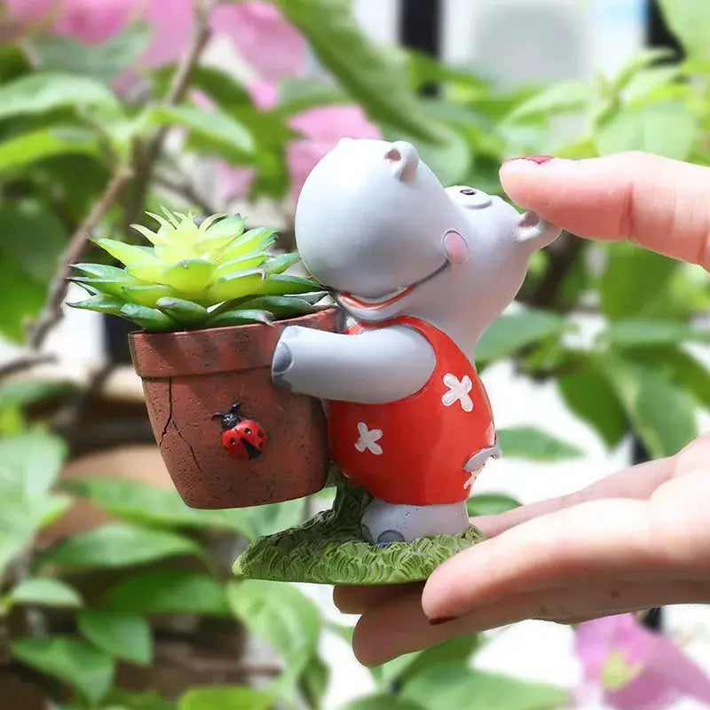 a small toy hippo holding a potted plant