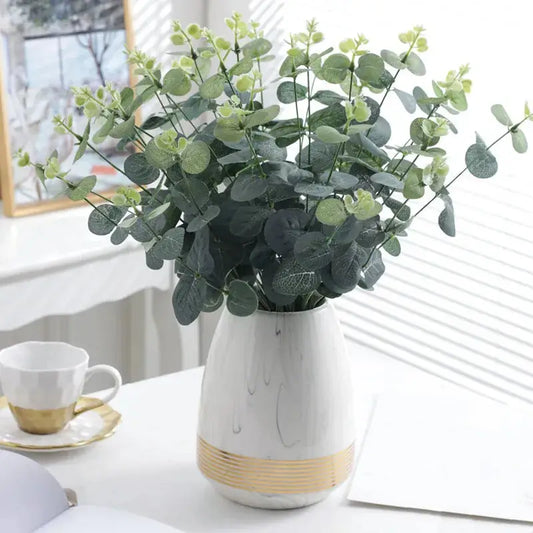 a white vase filled with green leaves on top of a table