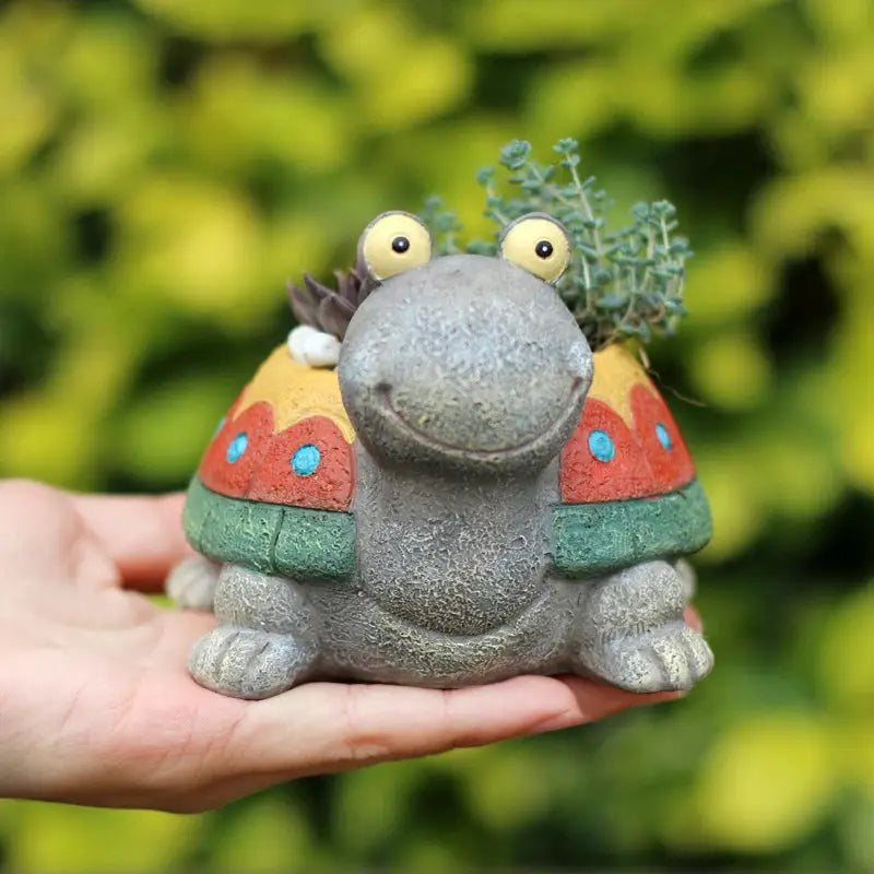 a hand holding a small ceramic animal with a plant in it's mouth