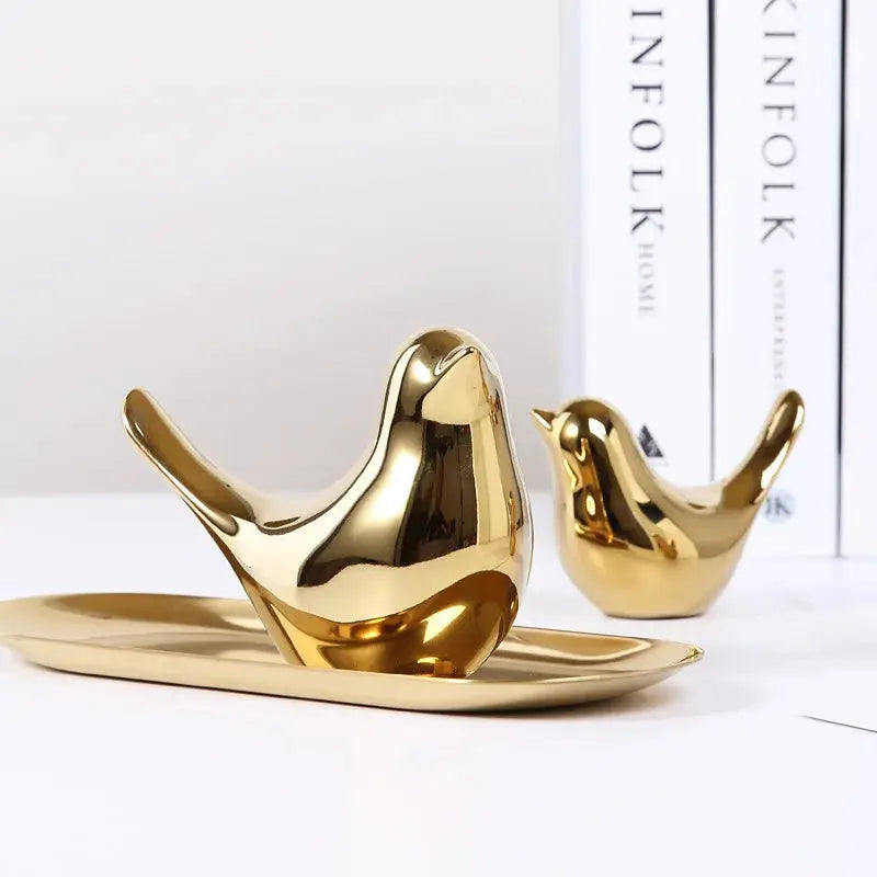 a couple of gold birds sitting on top of a white table