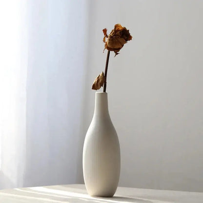 a white vase with a dried rose in it