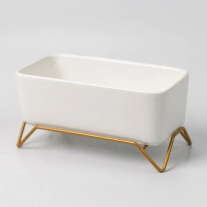 a white ceramic dish with gold legs on a white background