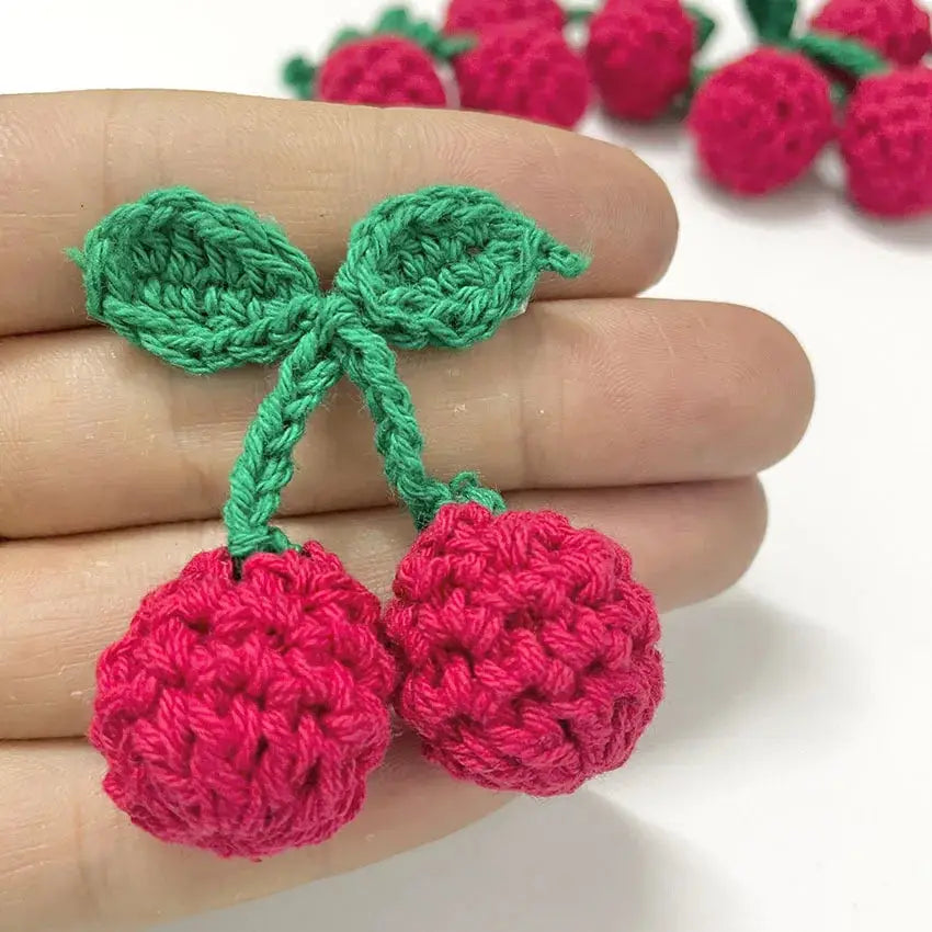 a hand holding a crocheted cherry ornament