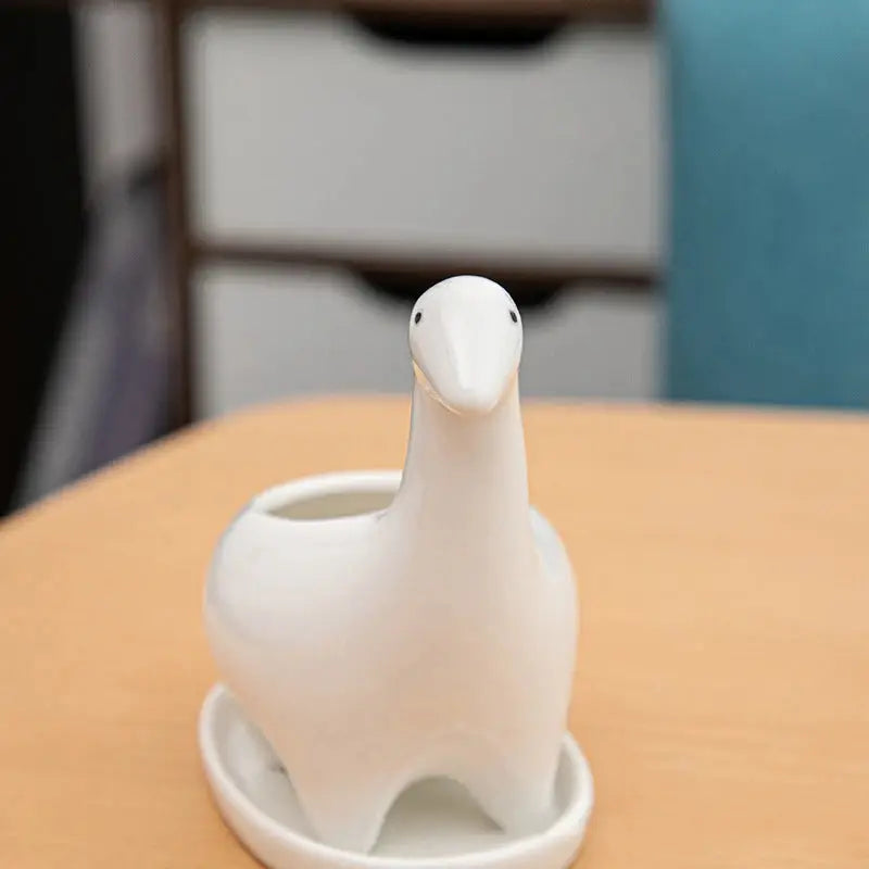 a white bird shaped vase sitting on top of a wooden table