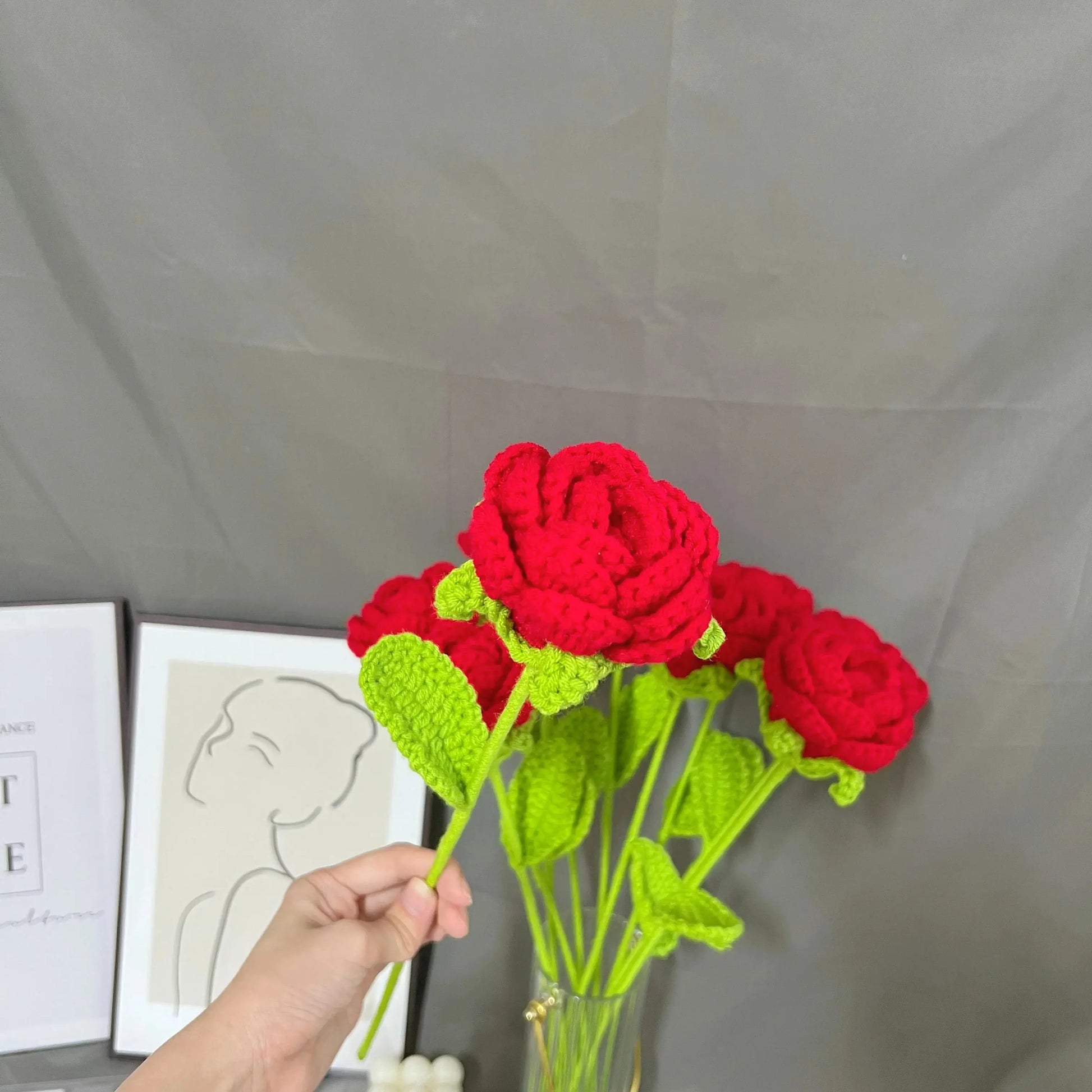 a hand holding a crocheted red rose in a vase