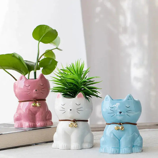 three ceramic cats with a plant in the middle