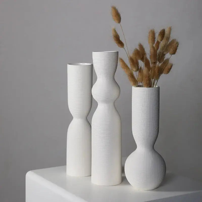 three white vases sitting on top of a white shelf