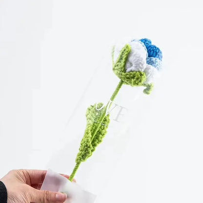 a hand holding a crocheted flower in a clear vase