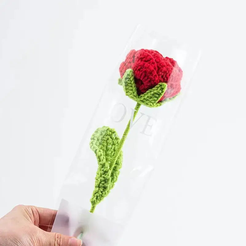 a hand holding a crocheted flower in a tube