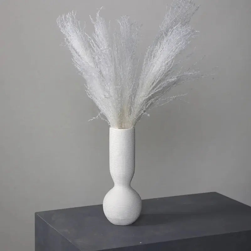 a white vase with some white feathers in it
