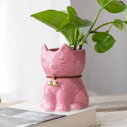 a pink ceramic cat planter with a green plant in it