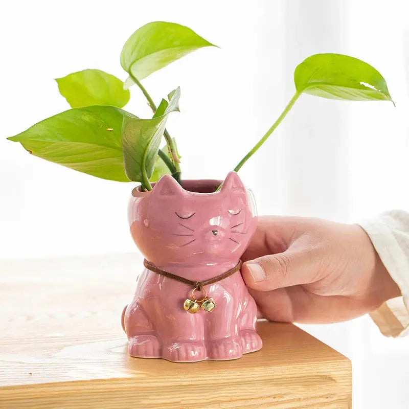 a hand holding a pink ceramic cat planter