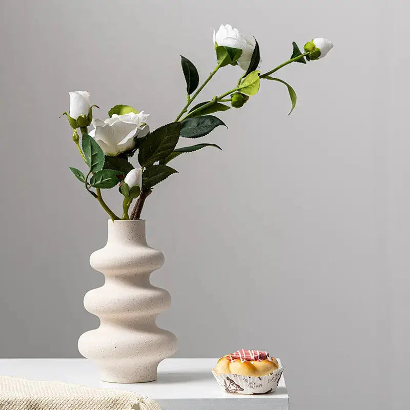 a white vase with flowers in it sitting on a table