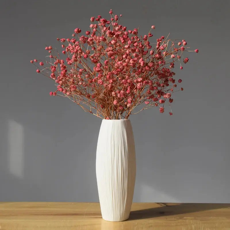 a white vase filled with red flowers on top of a wooden table