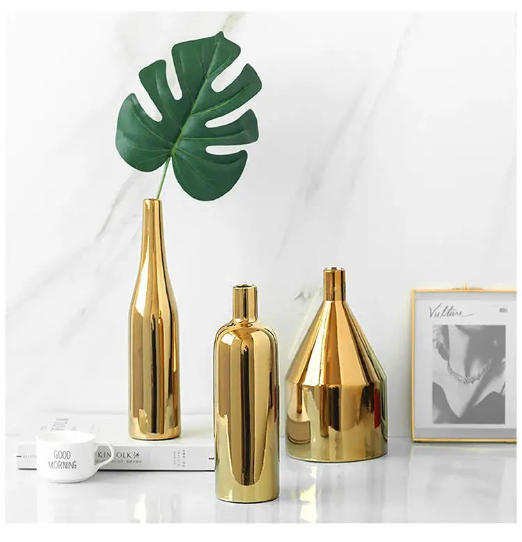 three gold vases and a green plant on a table