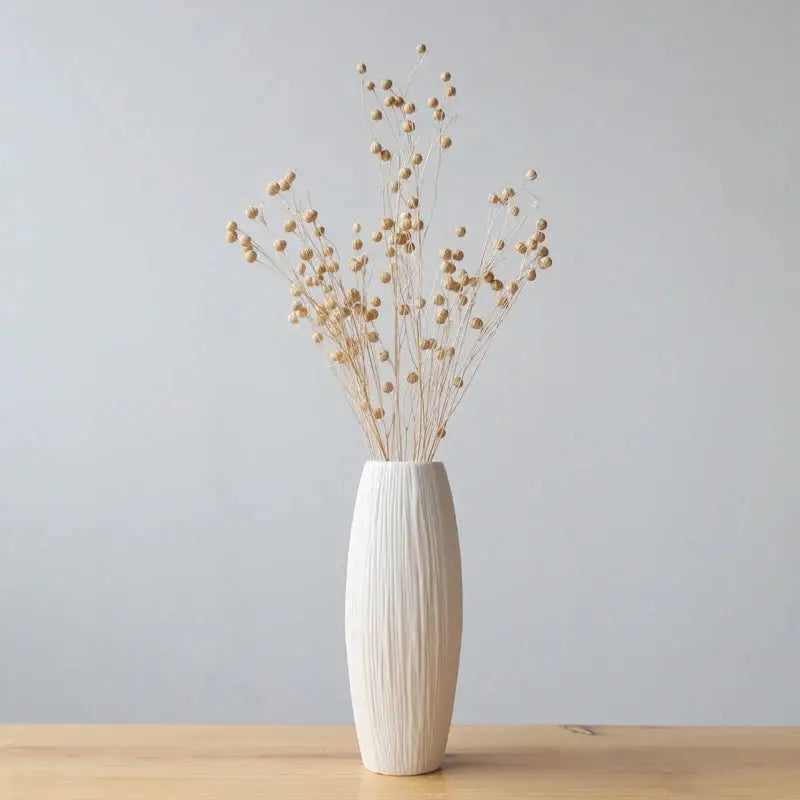 a white vase filled with dried flowers on top of a wooden table