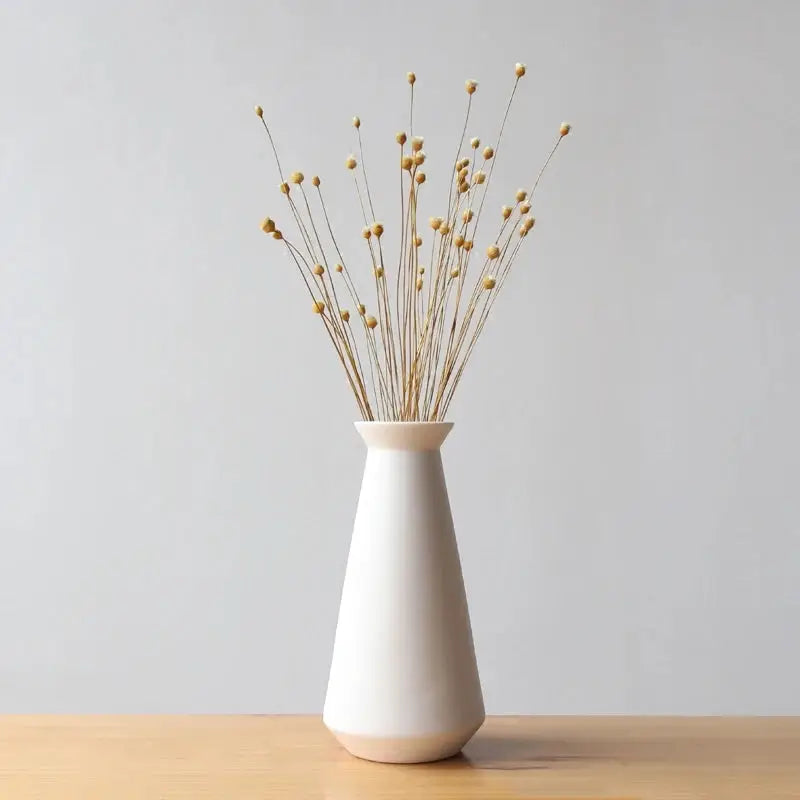 a white vase filled with yellow flowers on top of a wooden table