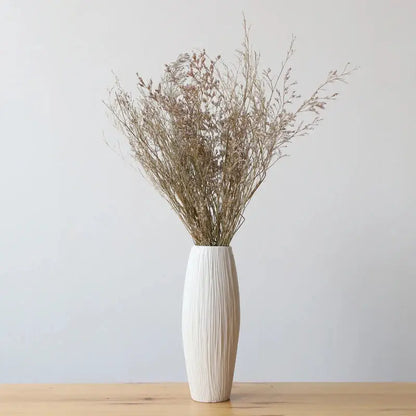 a white vase filled with dried plants on top of a wooden table