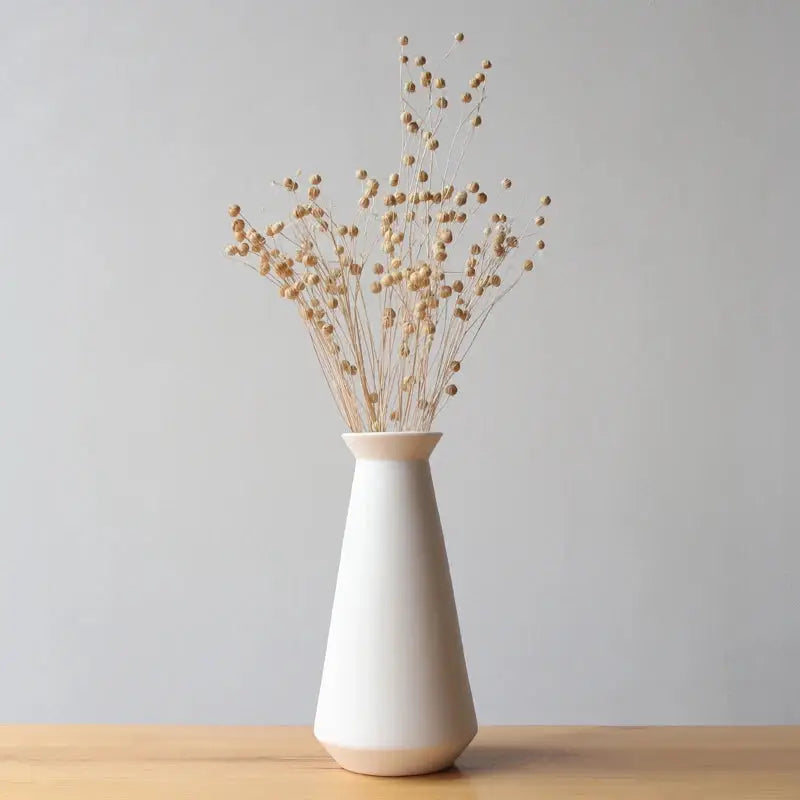 a white vase filled with dried flowers on top of a wooden table