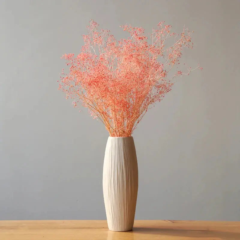 a white vase filled with pink flowers on top of a wooden table