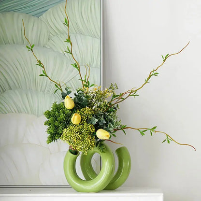 a green vase with yellow flowers and greenery