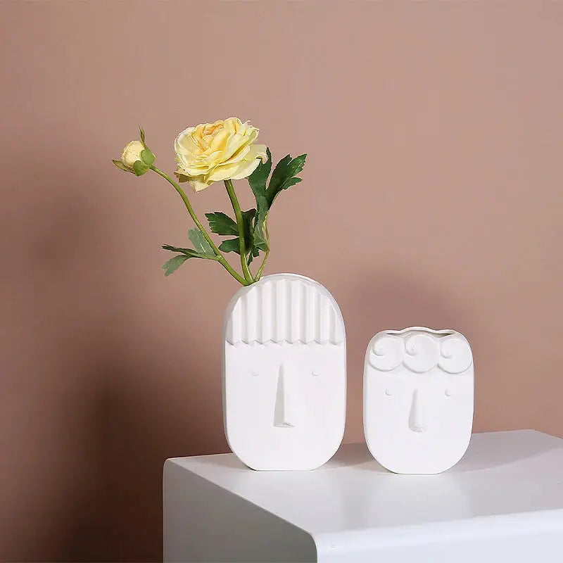 a white vase with a yellow rose in it