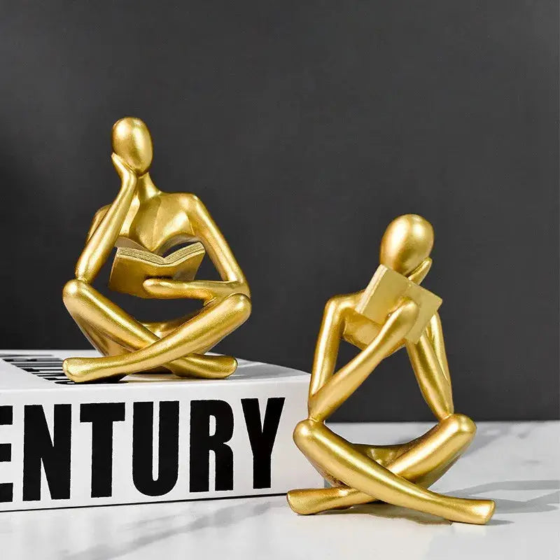 a couple of gold figurines sitting on top of a book