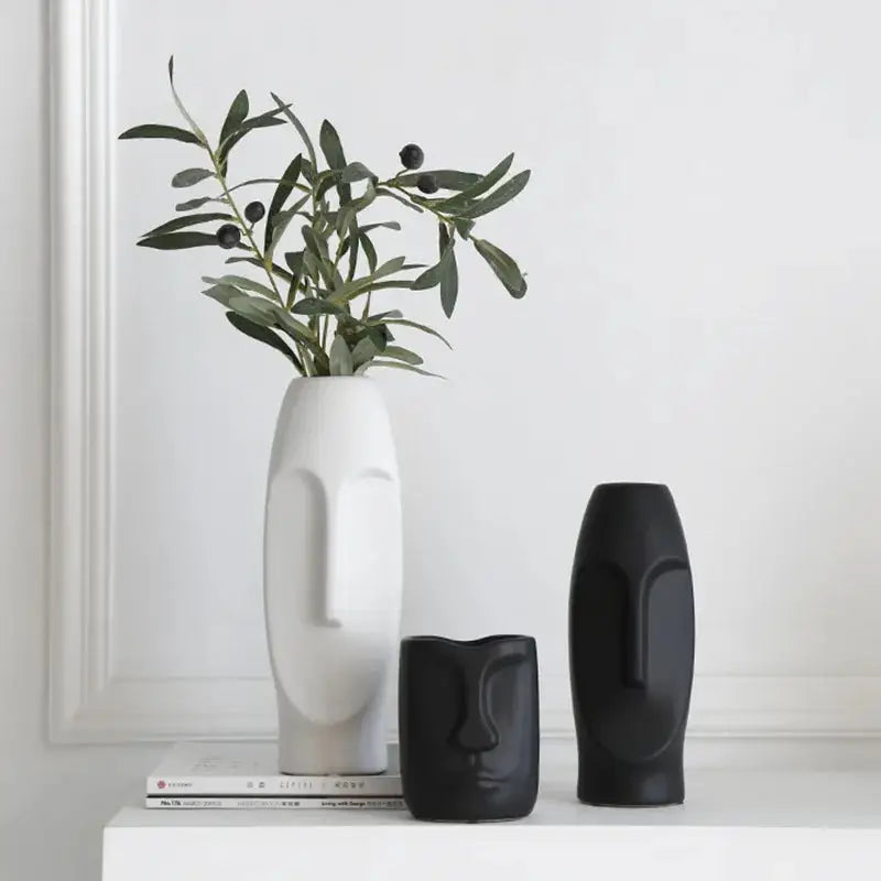 a white vase sitting on top of a table next to two black vases