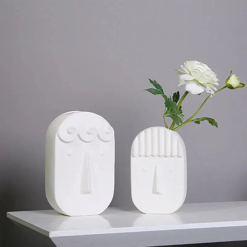 two white vases with flowers in them on a shelf