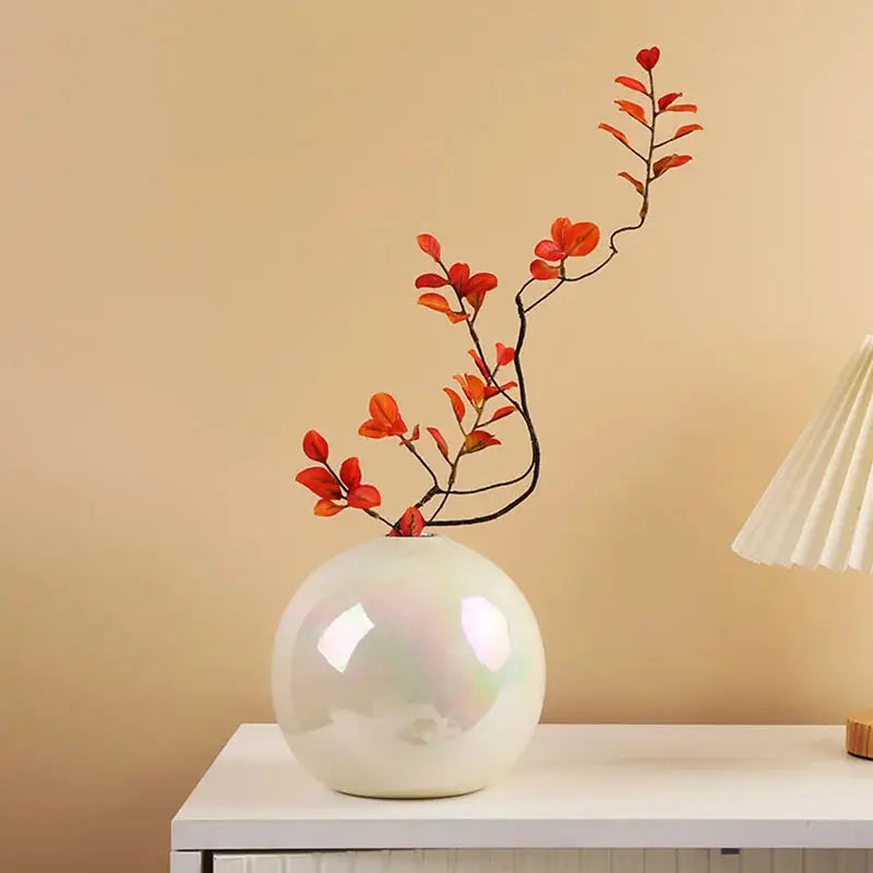 a white vase with red flowers on a white table