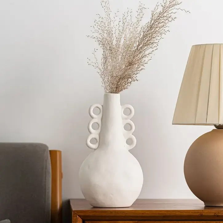 a white vase sitting on top of a table next to a lamp